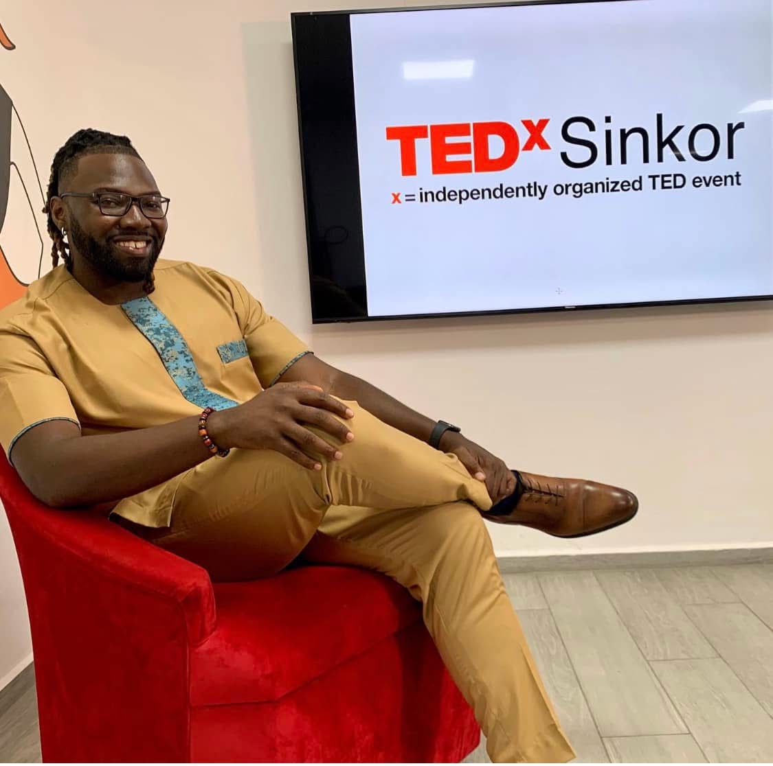 Lawrence seated beside the TEDxSinkor screen in Monrovia